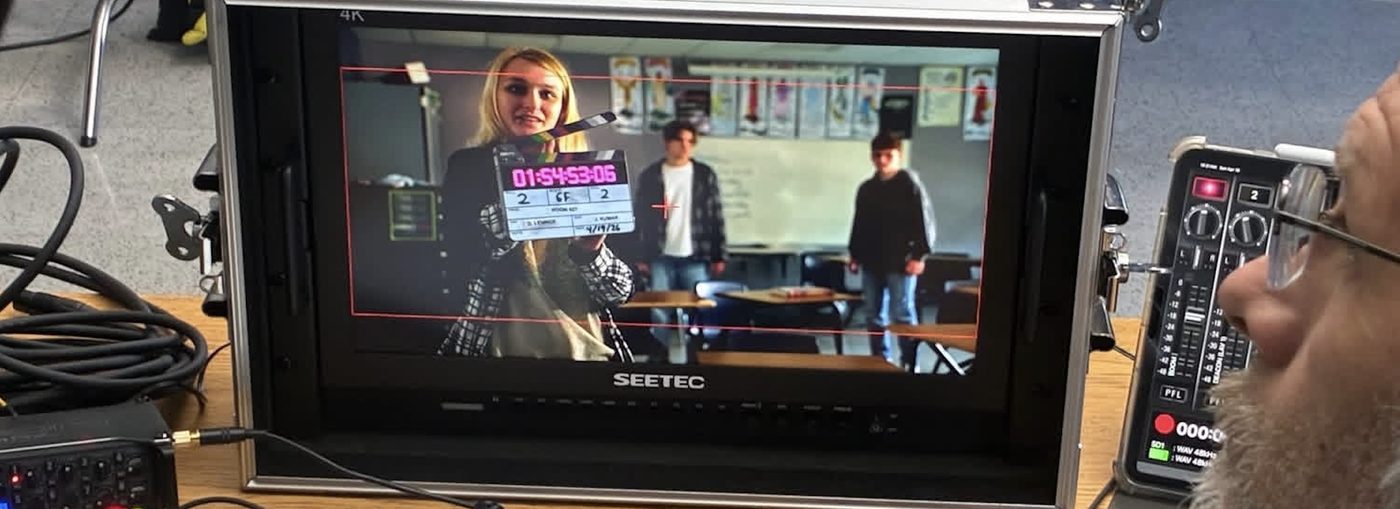 Behind the scenes on a Sycamore Films set: a director's monitor shows the framed shot as the clapperboard marks a take.